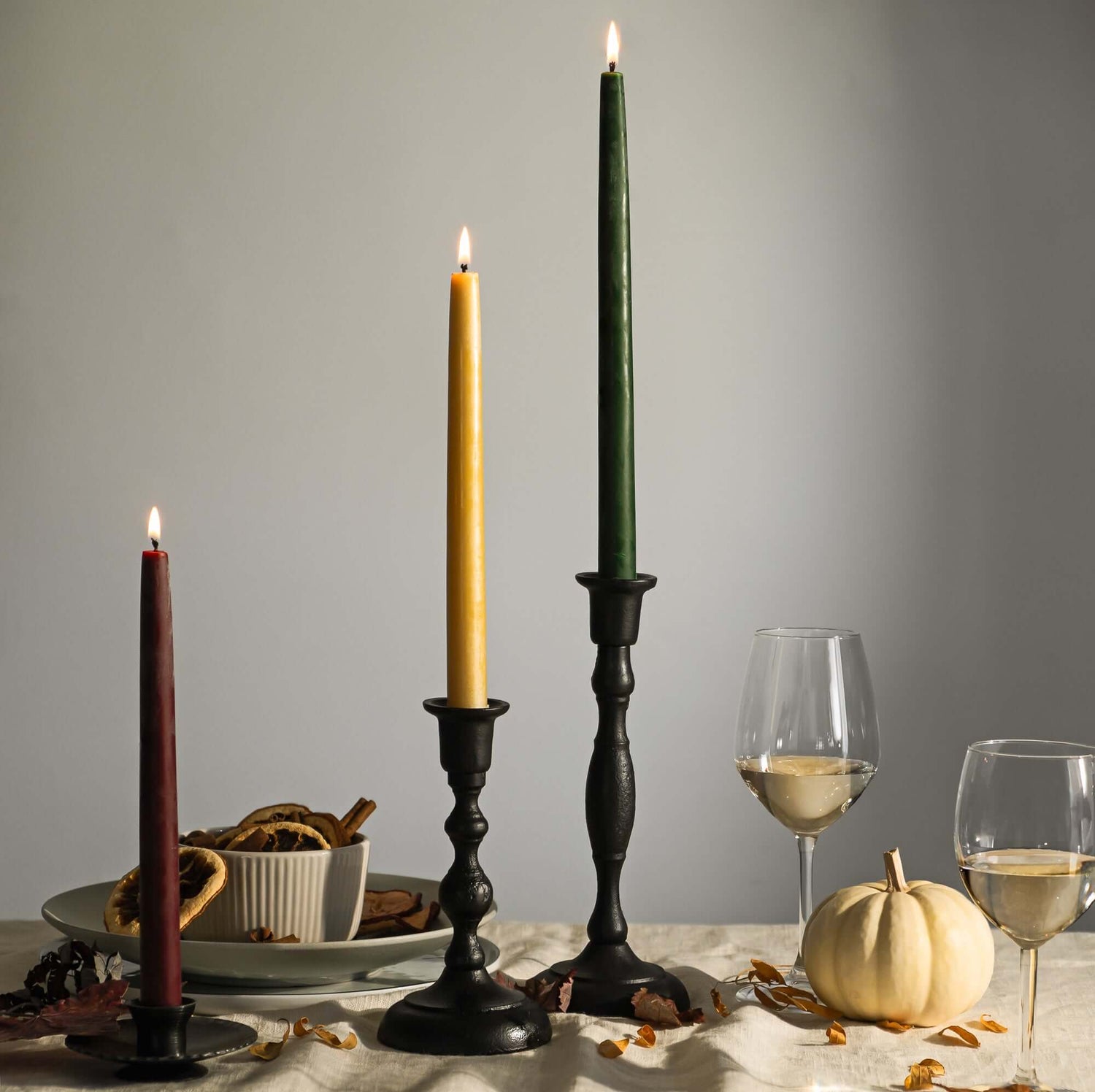 Decorative candles with candlesticks on a table with wine glasses and a pumpkin.