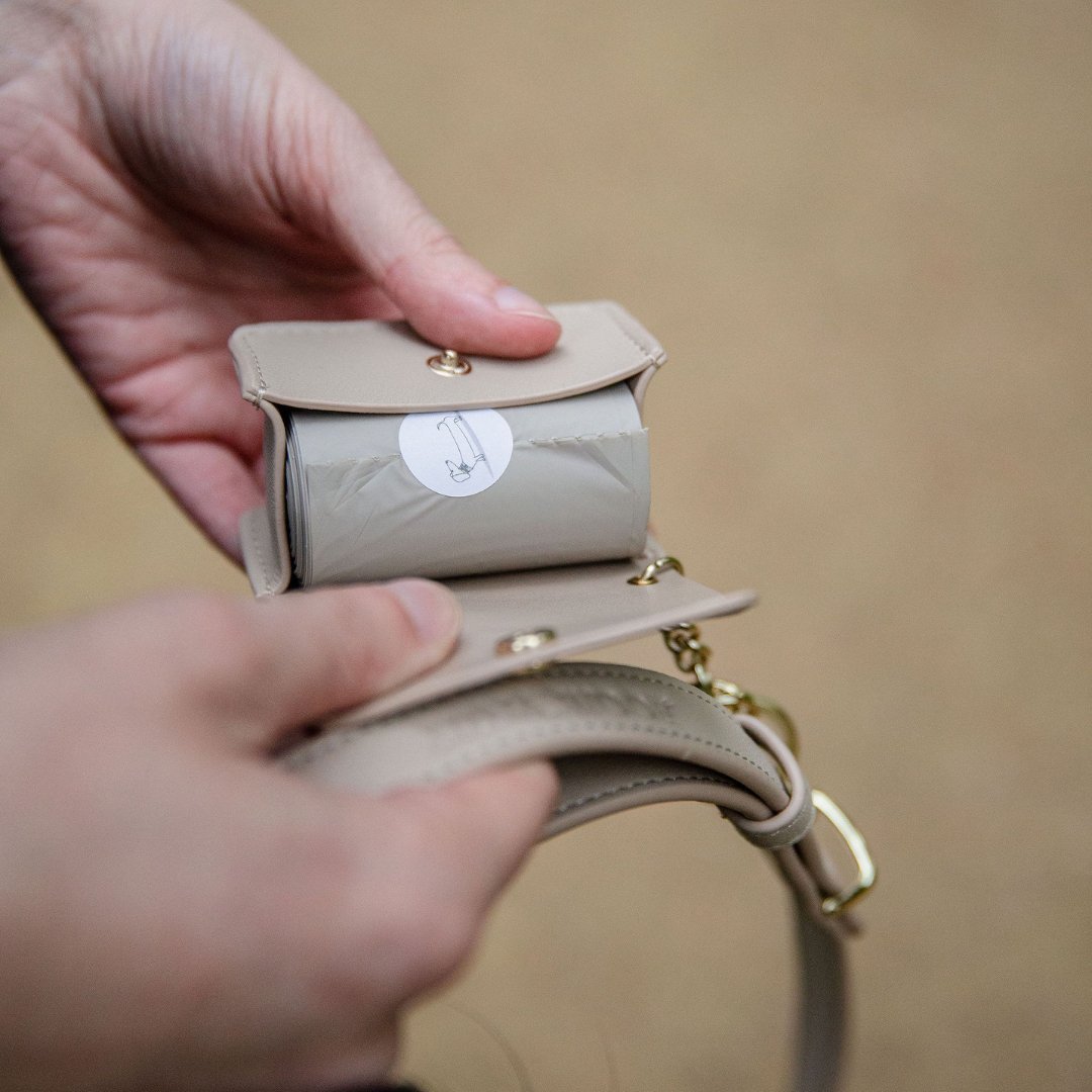 Beige vegan leather dog waste bag holder, held by a person against a beige background.