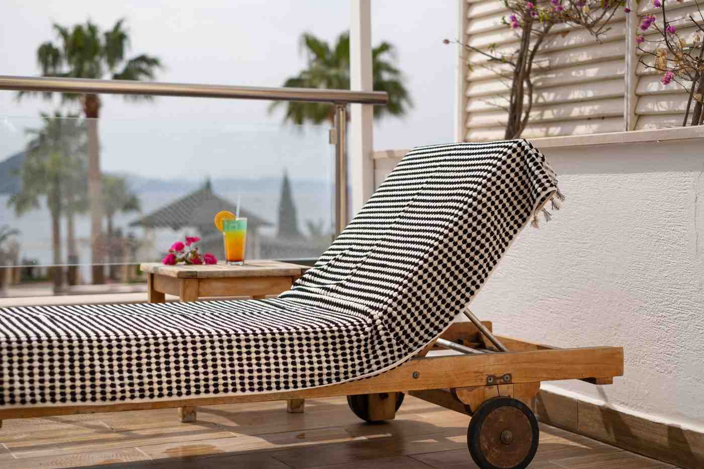 Wooden lounge chair with a black and white Premium Organic Turkish Jacquard Bath Towel on a balcony with palm trees in the background.