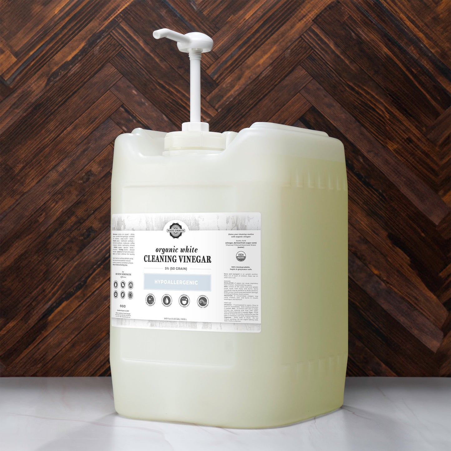 Large container of organic white cleaning vinegar with a pump against a wooden background