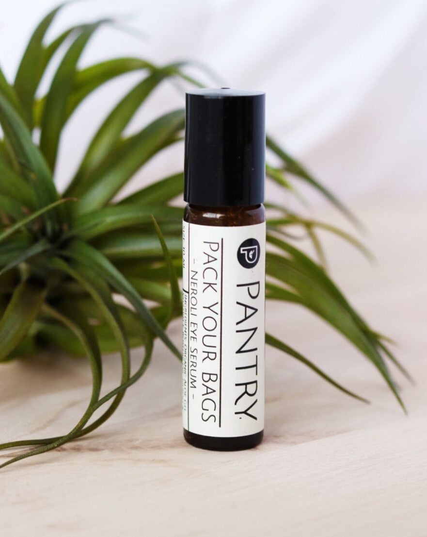 Roll-on bottle of 'Pack Your Bags' Organic Neroli Eye Serum by Pantry with a plant in the background. Vegan, Vegetarian, Gluten-Free, Cruelty-Free eye serum