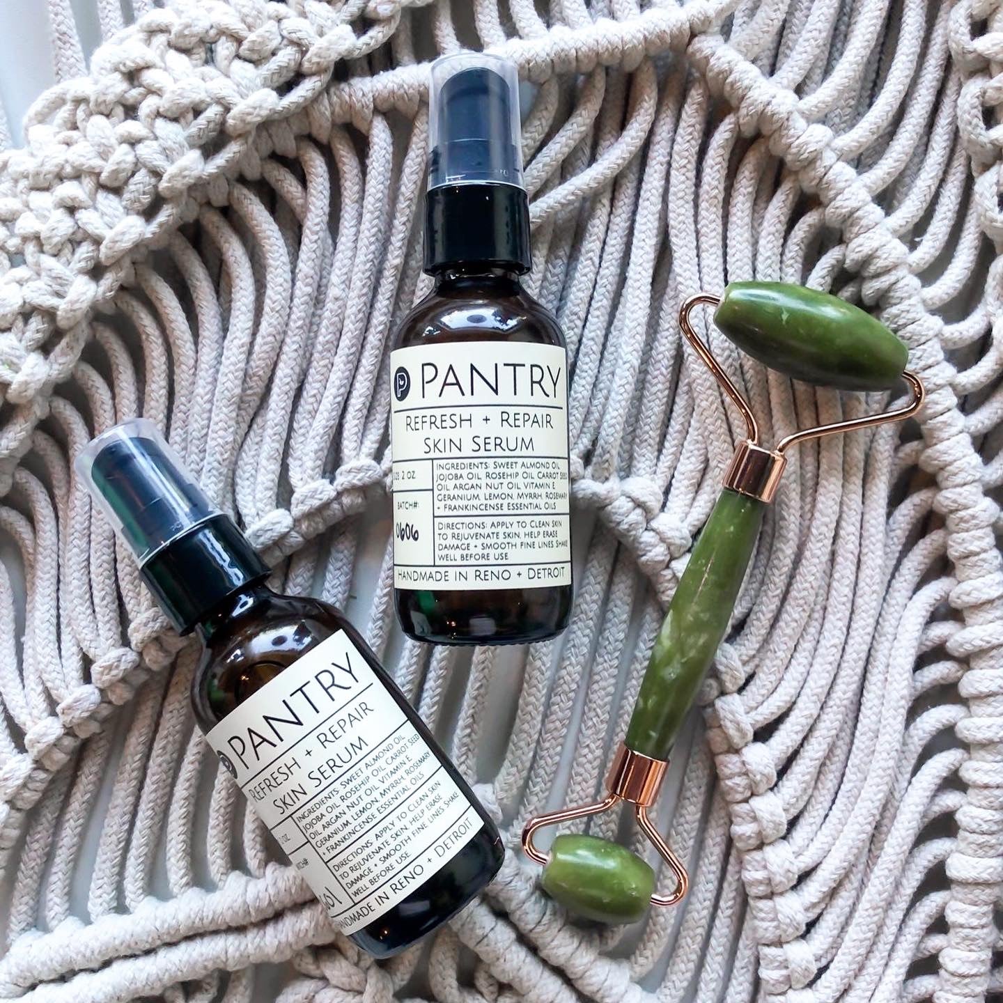 Two bottles of Pantry Refresh & Repair Anti-aging, Hydrating Skin Serum and a jade roller on a mesh bag.
