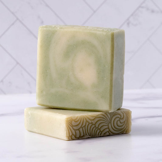 Two peppermint tea tree soap bars with a swirled pattern on a white surface with a light gray geometric background