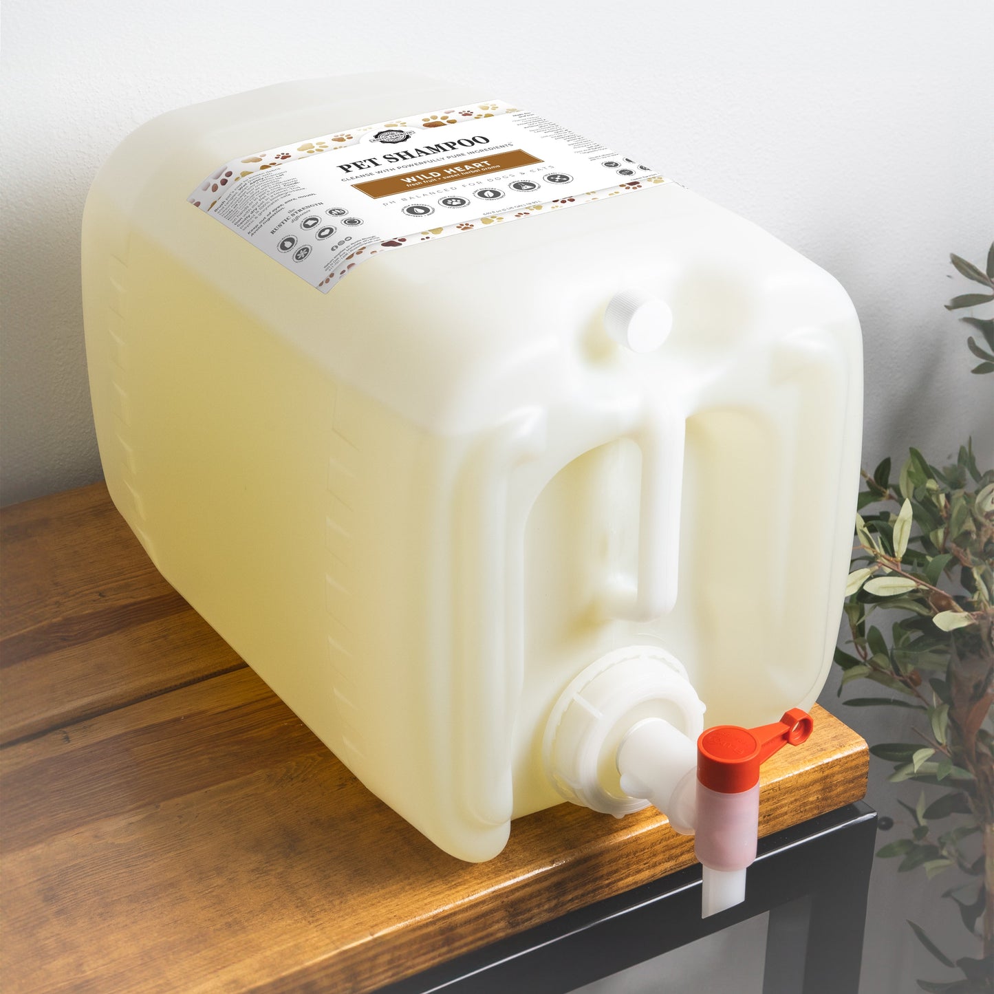 5 gallon white container of Rustic Strength pet shampoo with a red spout on a wooden surface