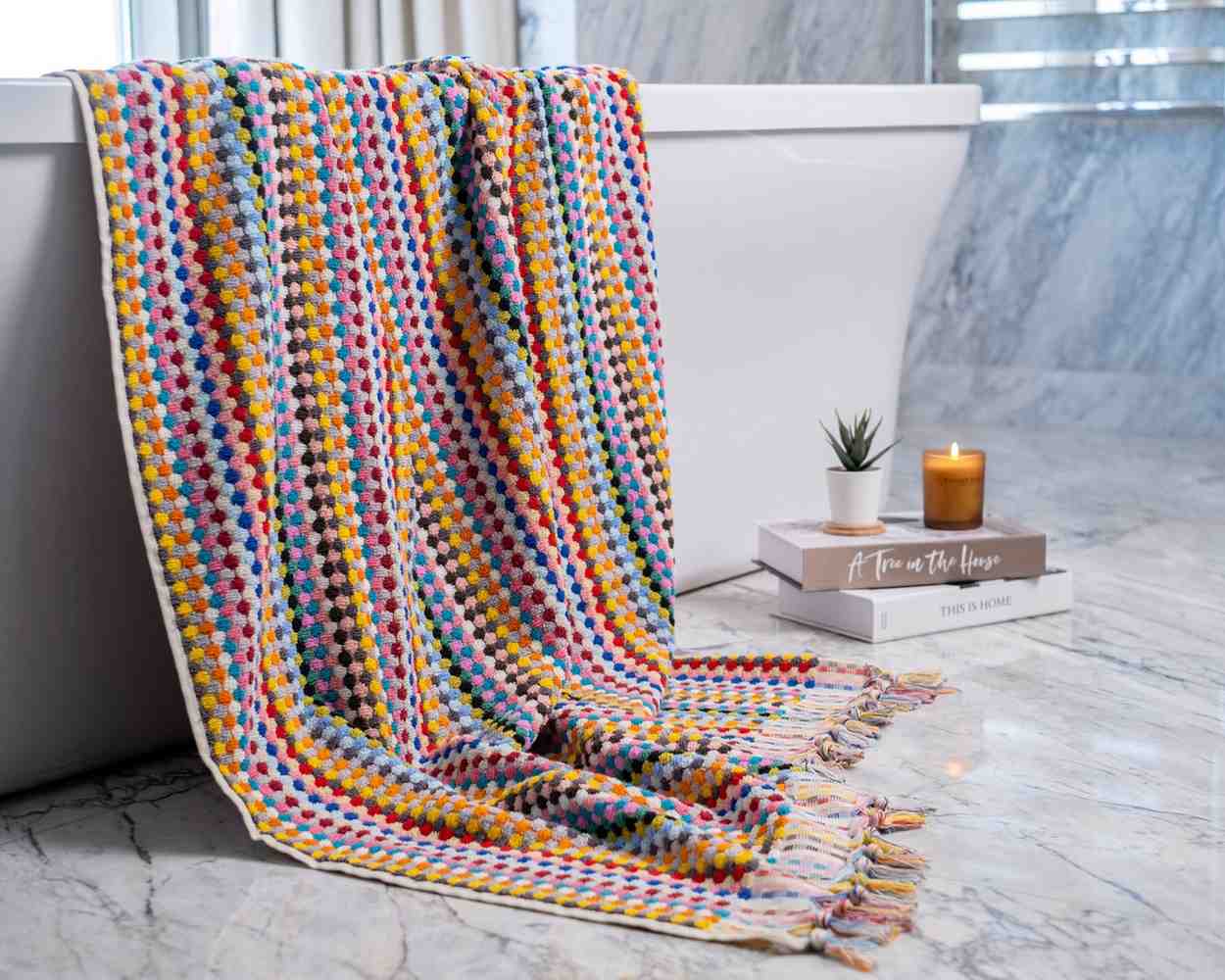 Colorful textured Premium Organic Turkish Jacquard Bath Towel draped over a bathtub with a candle and book on a marble surface.