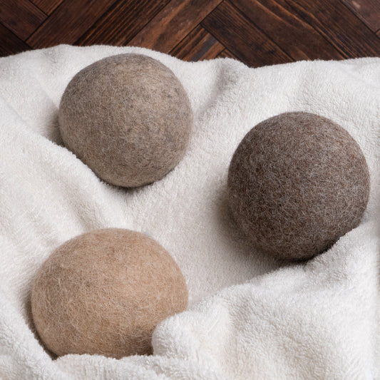 Three brown alpaca dryer balls on a white towel with a wooden floor background.