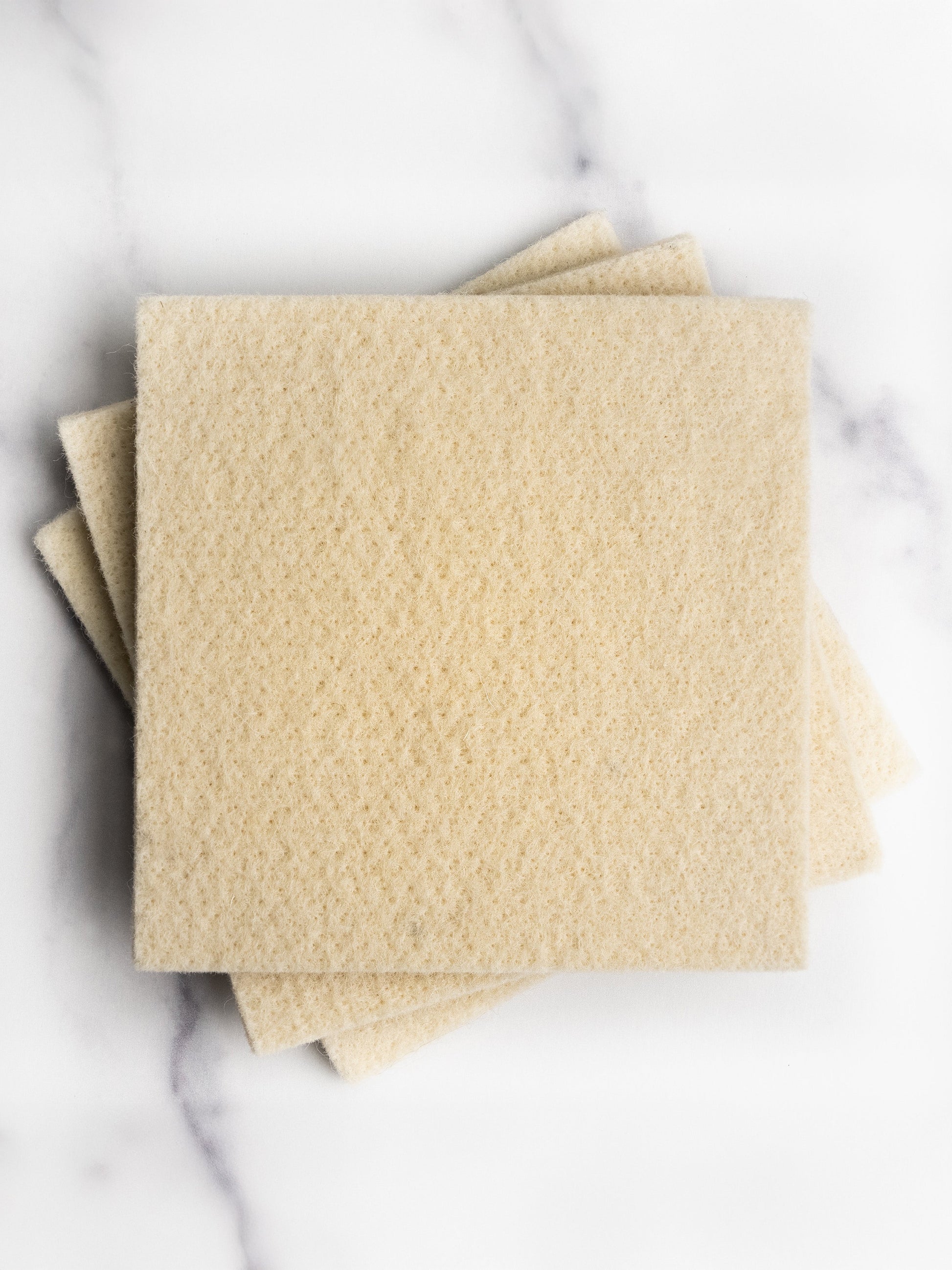 Three beige wool sponges on a marble surface