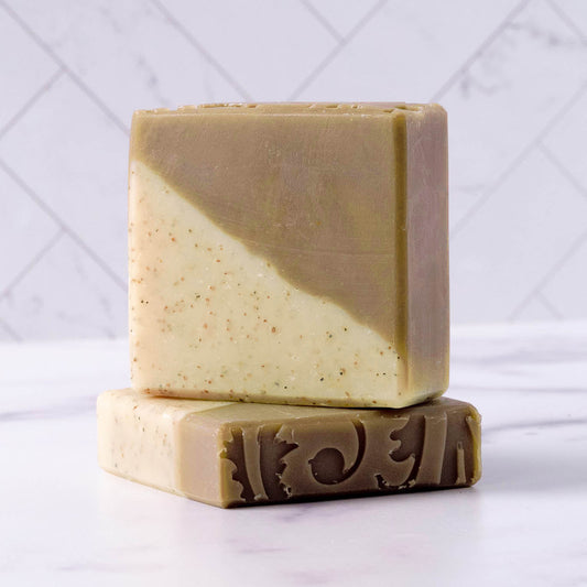 Two layered Sandalwood Patchouli soap bars stacked on a white surface with a light geometric patterned background