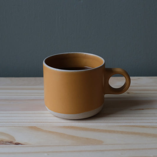 Handmade ceramic gold mug with a natural base on a blonde wooden surface and gray background. Made in the USA