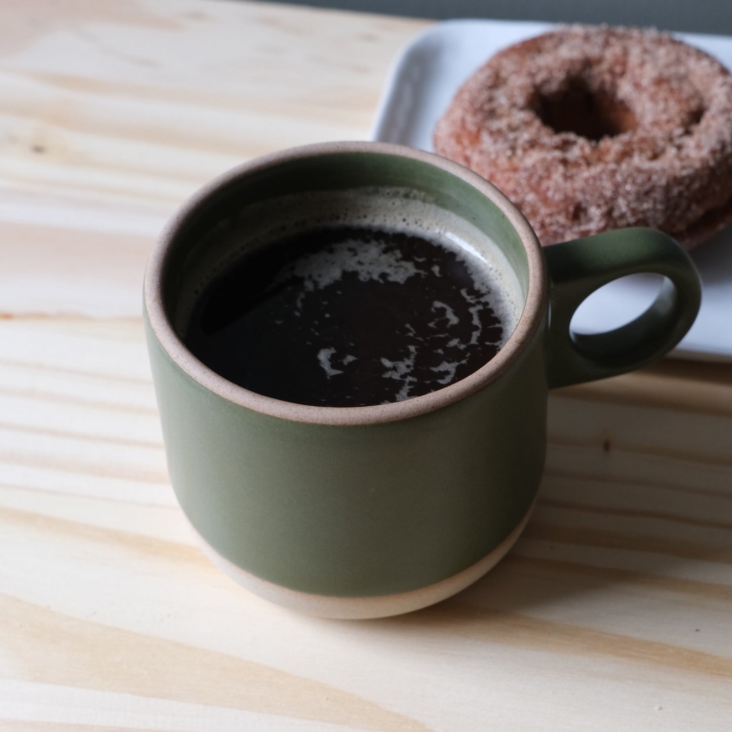 Handmade ceramic mug in green moss with coffee and a donut on a wooden table. Made in the USA