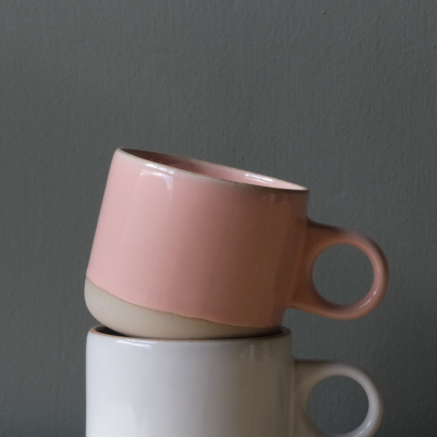 Two handmade ceramic mugs, one pink and one white, stacked against a gray background. Made in the USA
