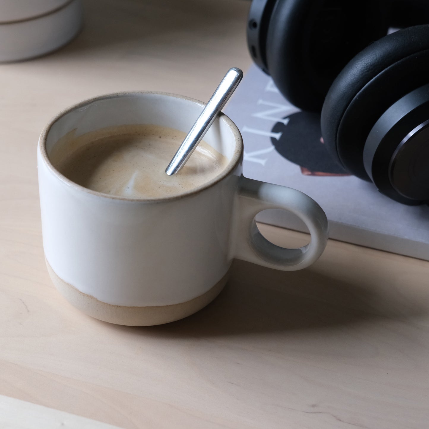 Handmade ceramic mug with coffee and spoon on a wooden surface next to headphones. Made in the USA
