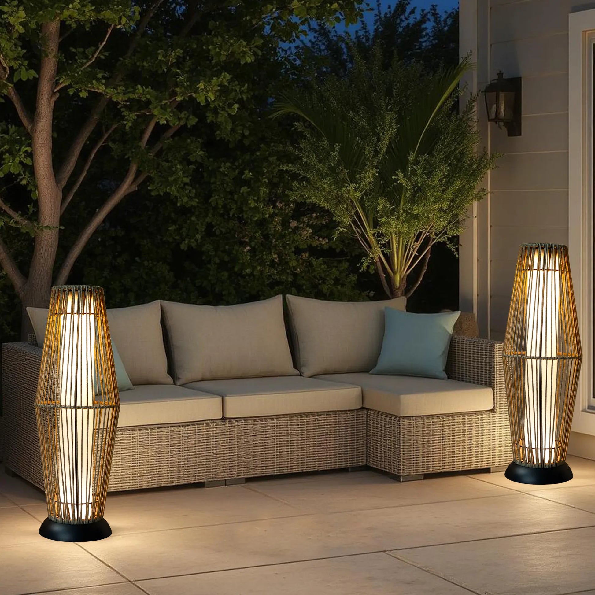 Outdoor patio with wicker sofa, floor two solar powered woven floor lamps, and evening sky.