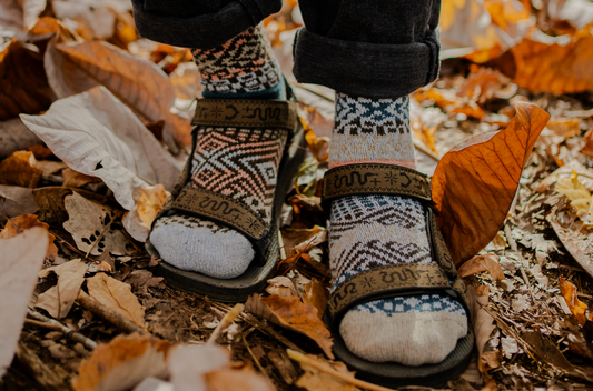 Madrona socks by Solmate, made with a blend of recycled merino wool, worn on feet standing in a pile of autumn leaves