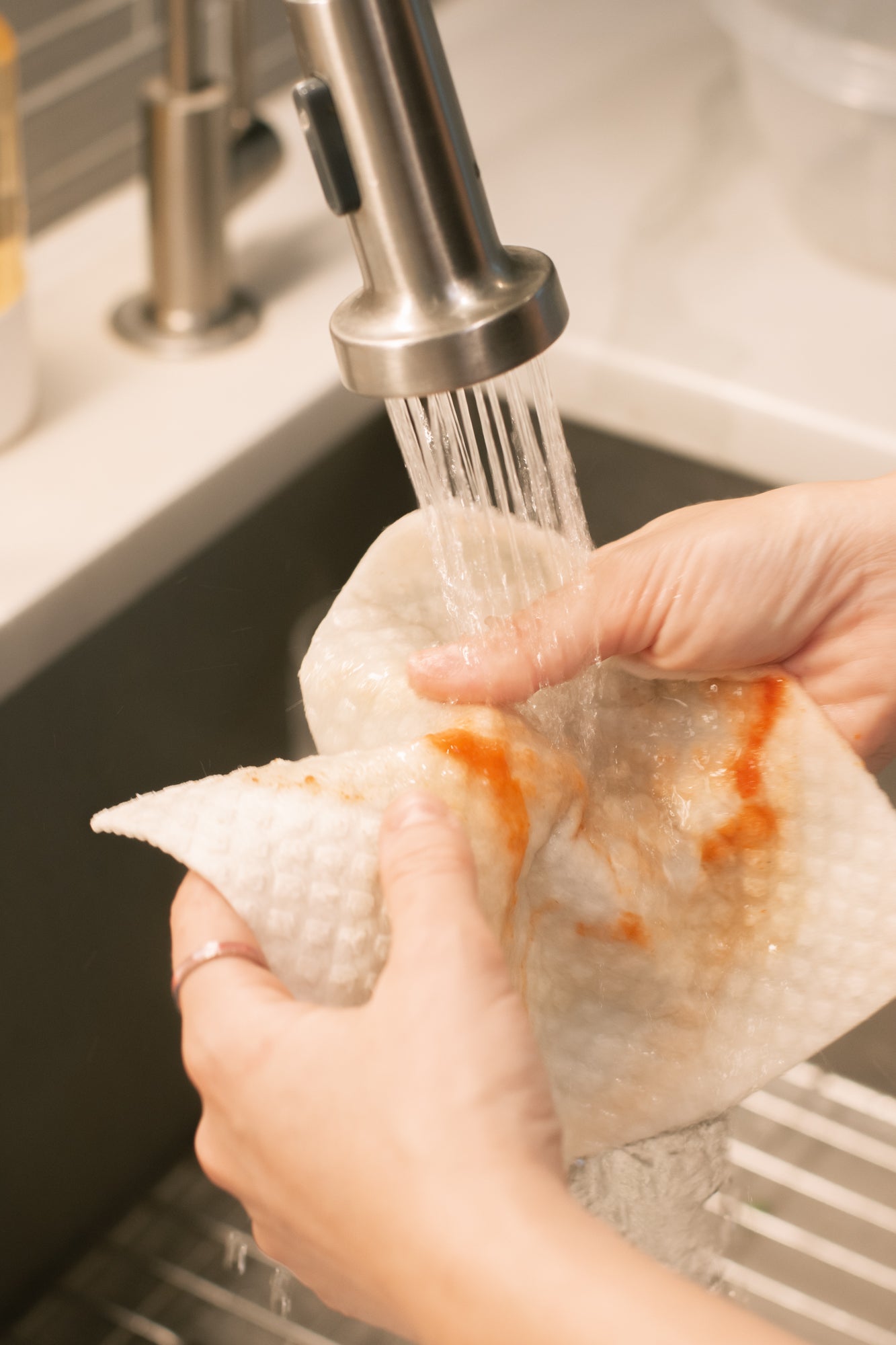 Person washing a paper towel with food residue under running water in a kitchen sink.