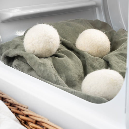 Three white dryer balls on a green towel inside an open dryer.